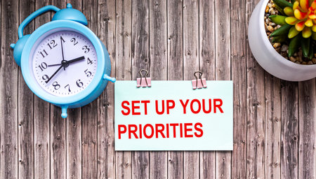 On a wooden table, an alarm clock and a cactus flower. On the sticker text Set up your prioritiesの写真素材