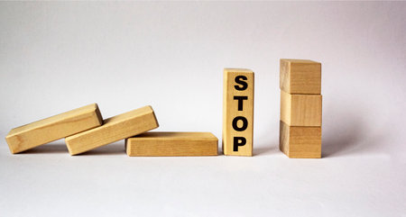 Concept of hand stop falling wooden blocks on a white background. On the block the word STOP.の写真素材
