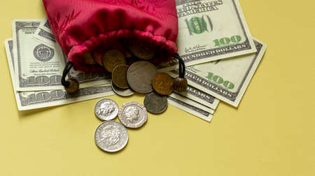 Old red bag with coins on a yellow background, there are dolars nearby
