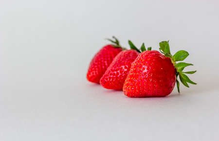 Three strawberries lie on a blue isolated background. There is a place to writeの写真素材