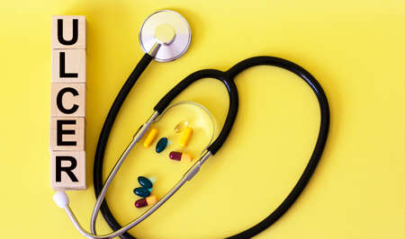 Ulcer inscription on wooden cubes. Section of medicine. A stethoscope and pills lie on a yellow...