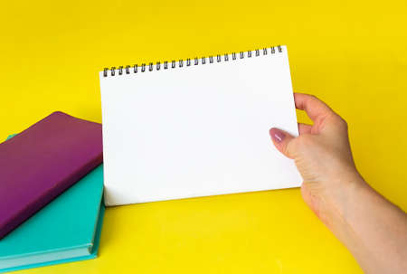 A female hand holds a large spiral notepad as a mockup for your design. Yellow background.の写真素材