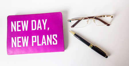 On a white background, a pen, glasses and a crimson notebook with the text NEW DAY, NEW PLANSの写真素材