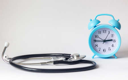 On a white background, a blue alarm clock with a stethoscope nearの写真素材