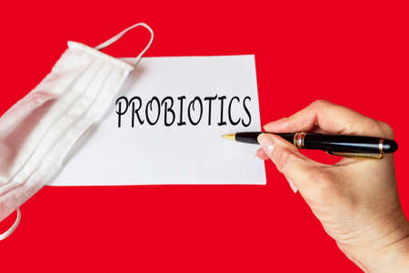 The word PROBIOTICS is written by a female hand on a notebook. A medical mask lies on a red background. The concept of medicineの写真素材