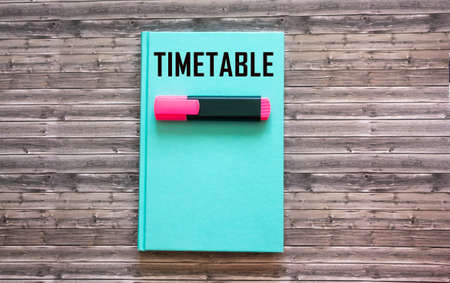 The word TIMETABLE is written on a green notepad and on a wooden background.の写真素材