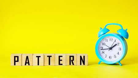 The word PATTERN is written on wooden blocks and on a yellow background, next to an alarm clockの写真素材