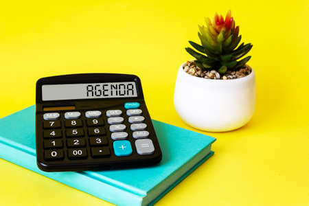 Agenda word on calculator and yellow background with diary and alarm clock. Business and finance concept.の写真素材