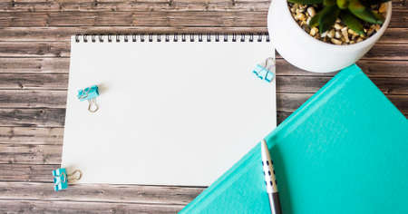 Wooden office desk with notepad, green diary, pen and flower.