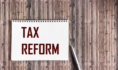 Tax reform, the text is written on a white notebook and a wooden table with a pen.の写真素材