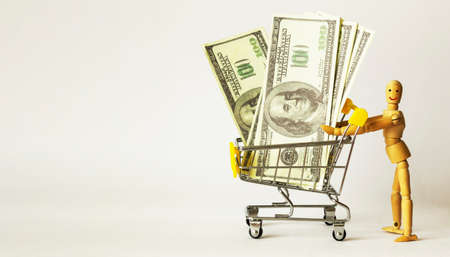 A wooden doll rolls money in a shopping cart