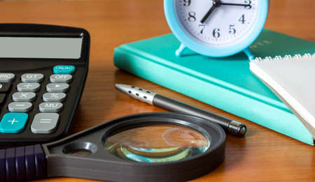 A desktop with a calculator, diary, magnifying glass, pen and an alarm clockの写真素材
