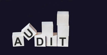 AUDIT word written on wooden block and black background