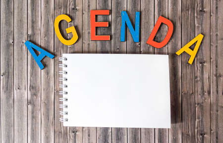 Of multicolored letters, the word AGENDA on a wooden table next to a blank notepad for writingの写真素材