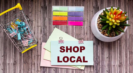 Shop Local text on paper label and wooden table. Beside a basket of paper clips and a cactus