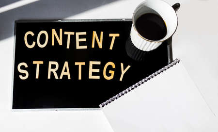 Content strategy word cloud on black background with notepad and coffee cup.