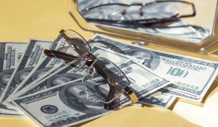 Dollars and glasses lie on a light background. There is a mirror in the background.の写真素材