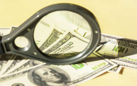 Magnifying glass and many hundred dollar bills with a portrait of President Benjamin Franklinの写真素材