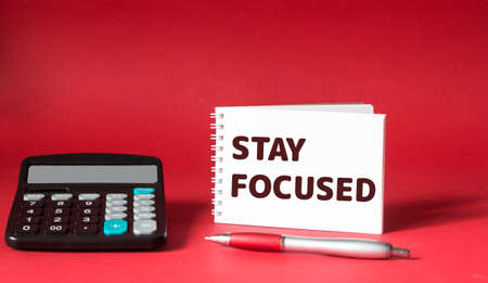 Stay focused reminder or tip-text on a notepad with a calculator and pen on a red background.の写真素材