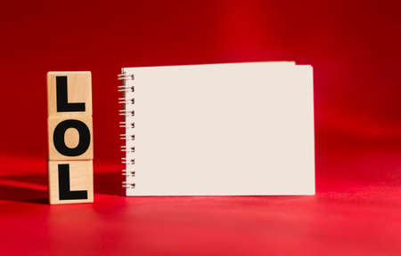 Wooden cubes with the text LOL on a red background and with a notepad for writingの写真素材