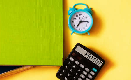 PATENT text written on the display of a calculator on a yellow background with a folder for documents and an alarm clock.の写真素材