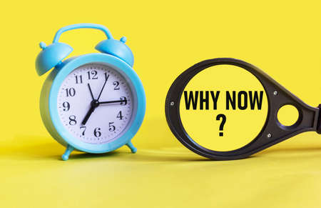 WHY NOW - written on a magnifying glass and yellow paper, next to a clock