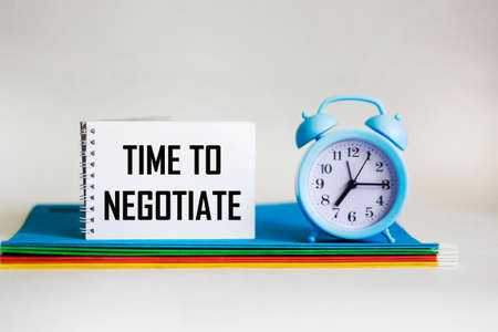 In a notebook, the text TIME TO NEGOTIATE next to multi-colored folders and a clock on a whiteの写真素材