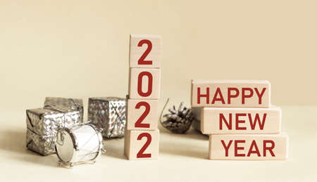 Text Happy New Year 2022 on wooden blocks and light background with gifts.