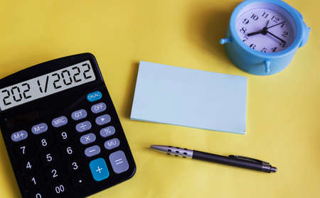 The text 2021 2022 on the display of a calculator. On a yellow background, a clock, a pen and a notebook for writing. Planning for the new yearの写真素材