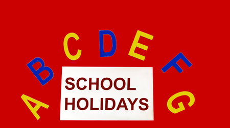 School holidays text written on a sticky note and on a red background with wooden alphabet letters in different colors.の写真素材