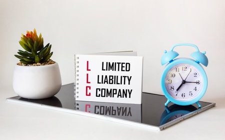 business and finance concept. On a white and black table there is a clock, a cactus and a notebook on which it is written - LIMITED LIABILITY COMPANYの写真素材