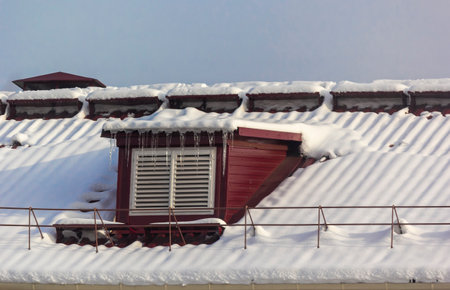 Large icicles on the roof of the house on a snowy winter day. Roof cleaning from snow and icicles.の写真素材