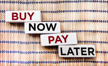 On a beautiful background are four wooden blocks with the words BUY NOW, PAY LATER.の写真素材