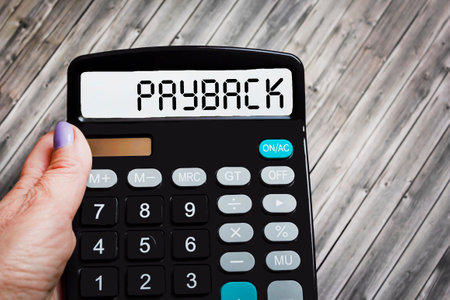 The word PAYBACK is written on a calculator in a girl's hand on a wooden table.の写真素材