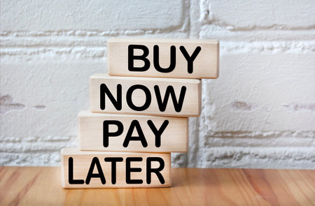 Against the background of a white brick wall, wooden blocks with the text BUY NOW, PAY LATER.の写真素材