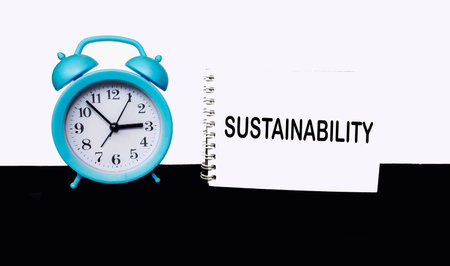 The word Sustainable Development is written on a notepad, next to a clock on a white and black background.の写真素材