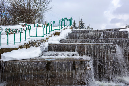 Winter landscape with stream and waterfall in a city park in Europeの写真素材