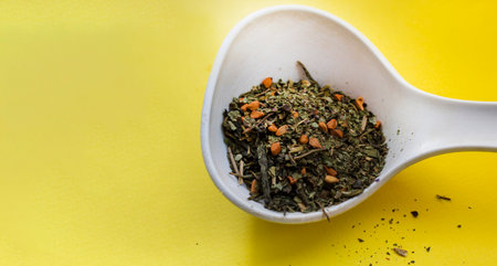 Ceramic white spoon with dry tea leaves and various berry additions on a yellow background