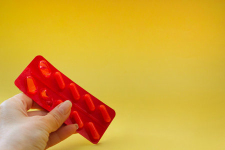 female hand holds medicines isolated on yellow background, offers medicines, helpsの写真素材