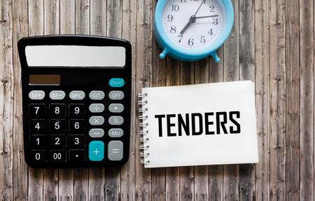 The word TENDER is written on a notepad, next to a calculator, a watch on a wooden background