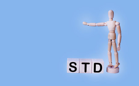 A wooden block forms the word STD on a blue background, with a wooden doll nearby. Healthcare concept..の写真素材