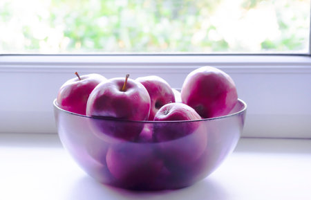 Red apples in a glass vase on the windowsillの写真素材