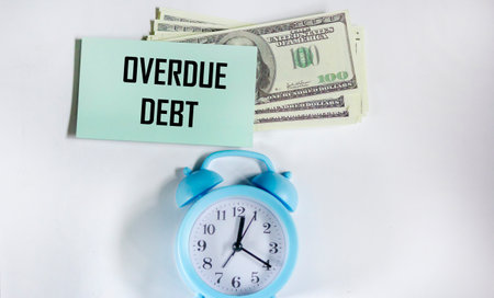 Notepad with the inscription OVERDUE DEBT, alarm clock and dollars on a white background. Business conceptの写真素材