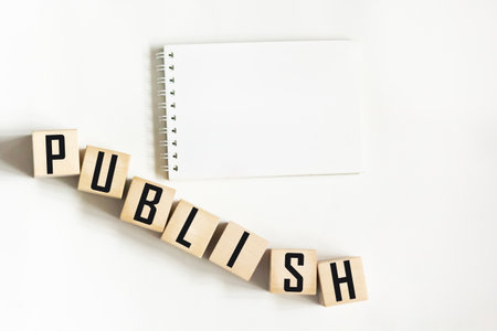 A white notebook on a white background. The word "PUBLISH" is written on wooden blocksの写真素材