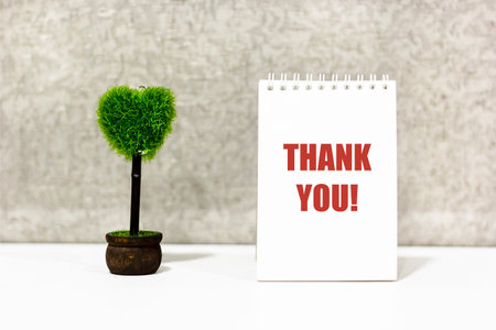 Words of gratitude on a notebook, next to a heart-shaped flower. Thank you