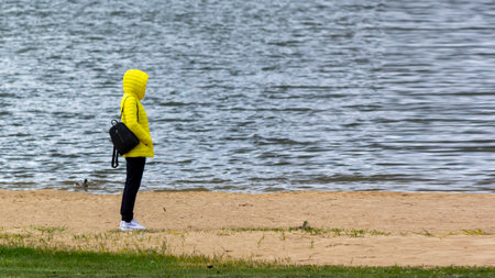 A girl in a yellow jacket stands on a sandy beach. She's wearing black sweatpants.の写真素材