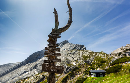 Wooden signpost in front of majestic mountains. Signs point to various hiking trails, including Hellenthal, Hohalm, Kreuzeck and Alpspitze.の写真素材