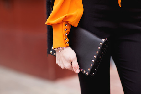 Street, office, bright style. Young woman, business style, black jacket, black pants, black handbag, sunglasses, orange blouse, belt, bracelet. Details.の写真素材