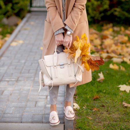 Stylish beautiful woman walking on the street wearing a beige coat, a bag, a warm sweater, a fashionable outfit, an autumn trend, accessoriesの写真素材