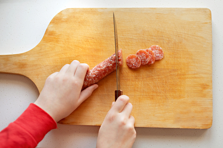Girl cooking, slicing salami on cutting board at the kitchenの写真素材
